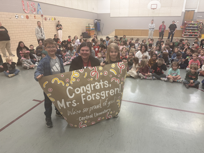 a teacher and two students holding a banner with students in the background