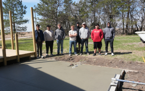 8 male students standing and smiling at a construction site